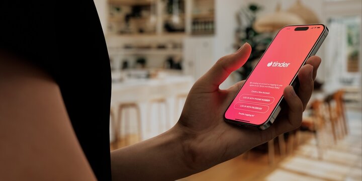 Hand holding a smartphone with Tinder app open, ready to swipe in a cozy home setting