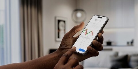 A user interacts with a stock trading app on a smartphone, displaying market charts and data, in a...