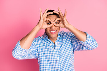 Photo of handsome funky guy wear plaid shirt showing arms binoculars isolated pink color background