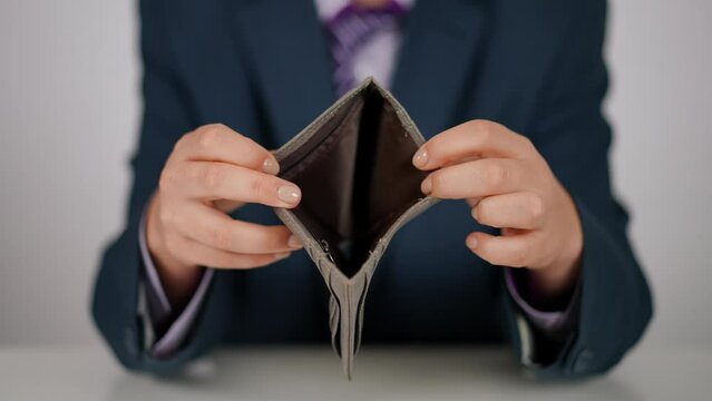 Close-up. An unrecognizable human in a blue suit and tie opens an empty leather wallet and shows its contents to the camera. Human posing while sitting at a white table indoors on a white background