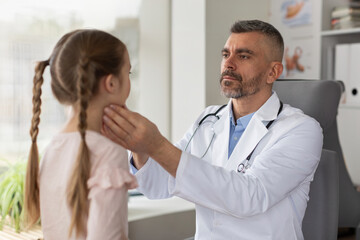 Professional male doctor examining little girl patient with thyroid gland problem in private clinic