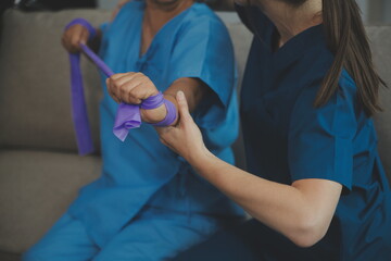 Personal trainer assisting senior woman with resistance band. Rehabilitation physiotherapy worker helping old patient at nursing home. Old woman with stretch band being coached by physiotherapist.