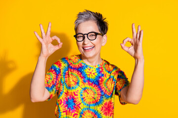 Photo of adorable nice lovely senior woman wear trendy print clothes okey sign isolated on vivid yellow color background
