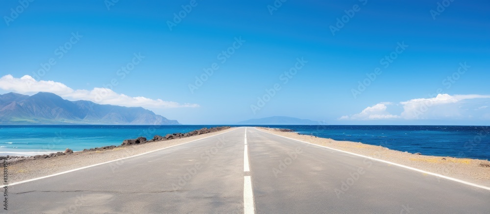 Poster an empty asphalt road with copy space image borders a serene beach under a clear blue sky.