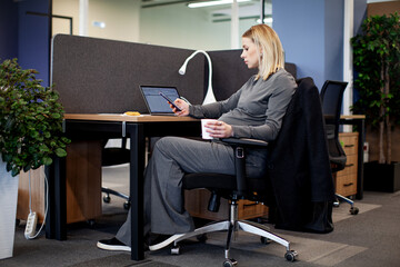 Pregnant woman sitting and working at a desk with a mobile phone in an office, with a computer and...