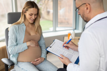 Pregnancy, medicine concept. Male gynecologist doctor writing prescription during visit of young...