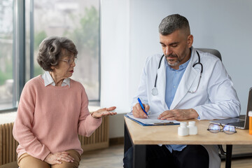 Senior woman on check up appointment with her doctor writing symptoms in flipboard and listening her. Checkup, prevention examination, diagnosis, medicine concept