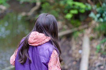 A little long-haired girl in a vest walks through the forest