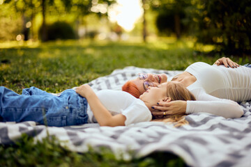 Beautiful mom and her daughter lying on a blanket at the park, head to head.
