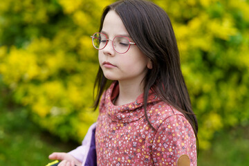 Little beautiful sad long dark haired girl with glasses on blurry green background