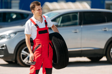 Young smiling man, in red coverall,  car mechanic holding auto tires
