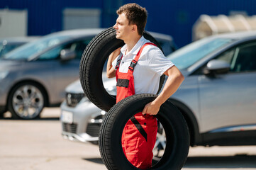 Young smiling man, in red coverall,  car mechanic holding auto tires