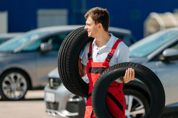 Young smiling man, in red coverall,  car mechanic holding auto tires