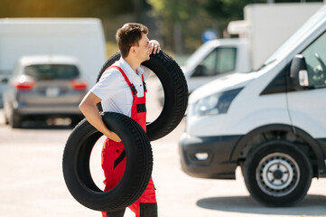 Young smiling man, in red coverall,  car mechanic holding auto tires