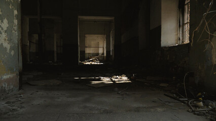 Abandoned, dilapidated building interior with debris scattered on the floor. Sunlight filters through the broken windows, casting shadows on the decaying walls and floor.