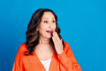 Photo of attractive senior woman cover mouth amazed look empty space dressed stylish orange clothes isolated on blue color background