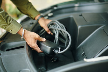 Hands of owner putting charging cable in trunk of hybrid car