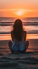 Fototapeta premium A young woman sits on the beach, watching the sunset