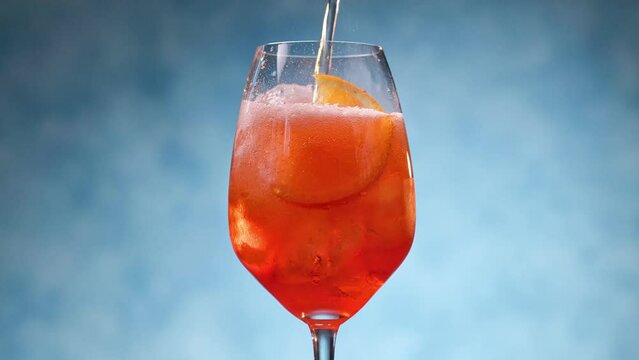 Glass of apperol spritz cocktail with orange slice on blue background. Closeup of summer drink, zoom in