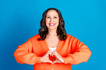 Photo portrait of attractive senior woman show heart gesture dressed stylish orange clothes isolated on blue color background