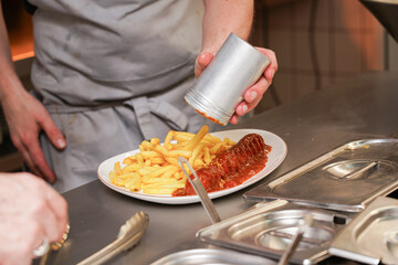 The cook prepares dishes from mashed potatoes and sausage with ketchup in a cafe.