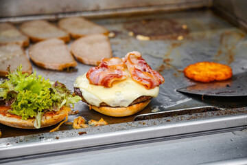 A burger with cheese, herbs and bacon is fried on the stove in a restaurant.