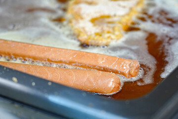Sausages and pork schnitzel are fried on a stove in a restaurant kitchen.
