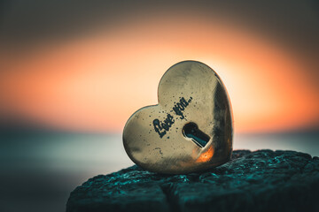 Old gold-colored lock in heart shape with the text love you on a wooden pole with the sunset on the...