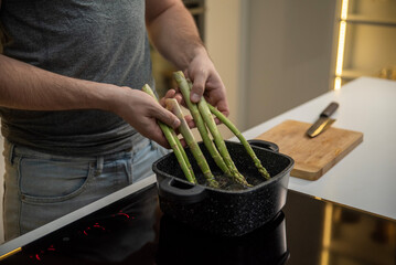 White man cooking asparagus in a stockpot on an induction cooker