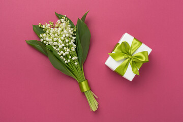 Lilies of the valley with gift box on color background, top view