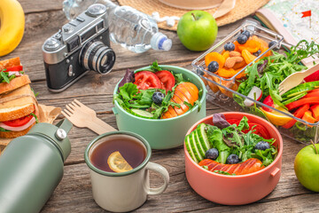 food travel lunch box with sandwich, vegetables, fruits and water on wooden table background, top view concept of vacation, tourism