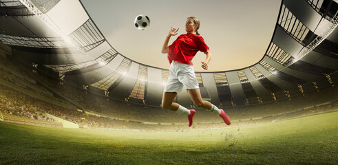 Dynamic image of competitive young woman, soccer player on field during game, hitting ball with...