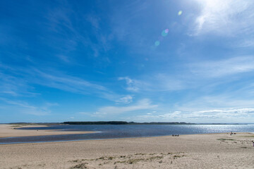 Panoramic view over water and beach of the lagoon Laguna de Rocha near La Paloma, Rocha, Uruguay with some people on the beach and sun shining bright above in blue sky