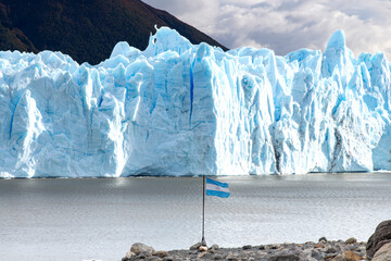 Rock formations with Argentinian flag in pole and water of lagoon at the white and blue colored...