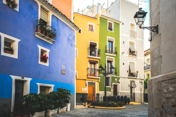 Obraz premium View to beautiful narrow Villajoyosa street with multi-colored houses. La Vila Joiosa - coastal town, Valencian Community, Spain, by Mediterranean sea