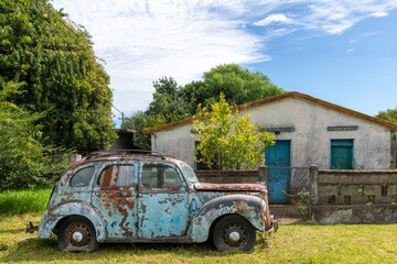 Wreck of a blue rusted vintage American car standing in front of abandoned house in Garzon, Uruguay...
