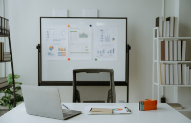 Close up view of simple workspace with laptop, notebooks, coffee cup and tree pot on white table with blurred office room background