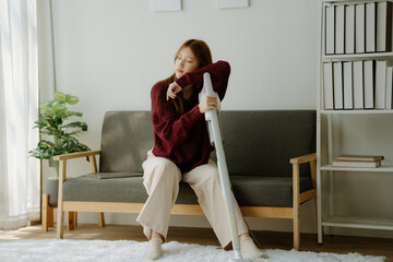 A woman in a purple sweater is standing in front of a white vacuum cleaner. She is tired and is...