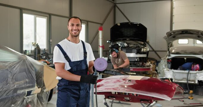 Professional auto mechanics working on a red car bumper with a grinding machine in an automobile repair service station. Focus on repair, renewal, and polishing.