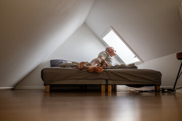 Tisvilde, Denmark A man sits on the bed in the  interior of an attic bedroom with a bed and a mansard roof.