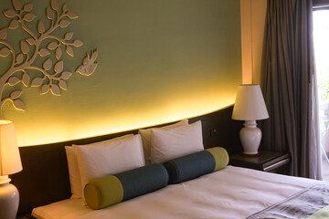 Bed and leaf-shaped headboard with light from below and white bedside lamps in a luxury hotel in...