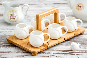 White porcelain coffee cups on a bamboo tray and a bird figurine on a white wooden table.