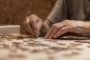 Dementia prevention. Elderly man hands doing jigsaw puzzle at home