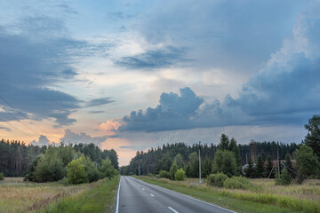 An empty road stretches through a verdant forest, disappearing into the distance under a stunning...