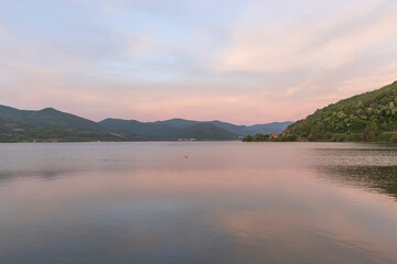  A serene sunset over a tranquil lake with rippled water, mountains in the distance, and a clear sky with soft clouds