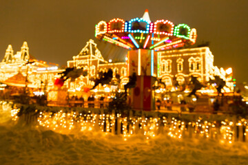 Defocused photo of people riding colorful carousel on Christmas Fair in winter with lots of lights and bokeh on snowy evening