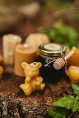 Handmade candles from natural beeswax in the shape of bear, pine cone and others, jars of honey. Hobby. Beekeeping. Artistic photo of beekeeping products against the backdrop of nature, forest
