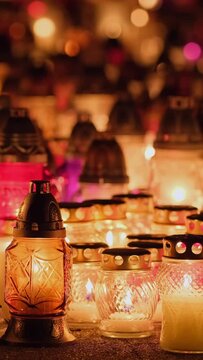 Candle lights on graves and tombstones at a cemetery in Poland during All Saints Day, Zaduszki day, and Day of the Dead. Lit candles illuminate the graves at a Christian cemetery at night.