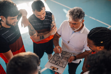 High angle view of a diverse male basketball team and elderly coach in huddle