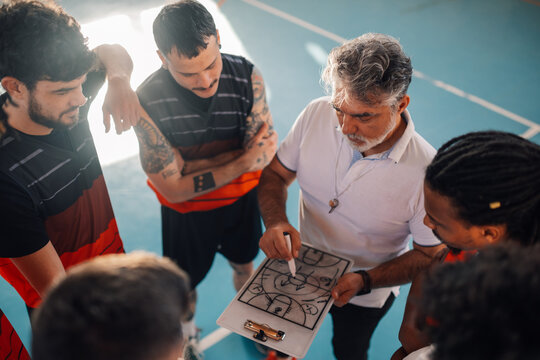 High angle view of a diverse male basketball team and elderly coach in huddle